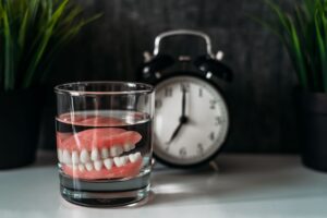 Dentures in a glass of water on a table next to an analog alarm clock